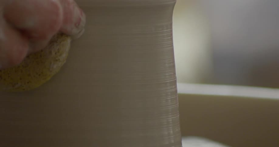 A wet sponge is applied to the surface of a vessel rotating on a pottery wheel
