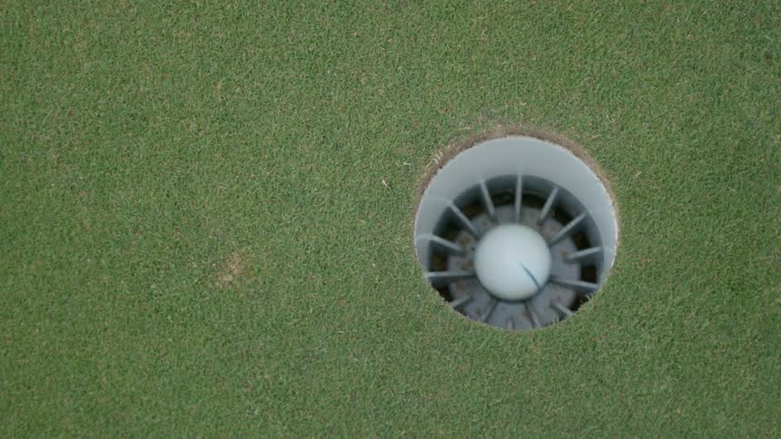 Golf ball enters a hole in the golf course and a hand immediately picks it up
