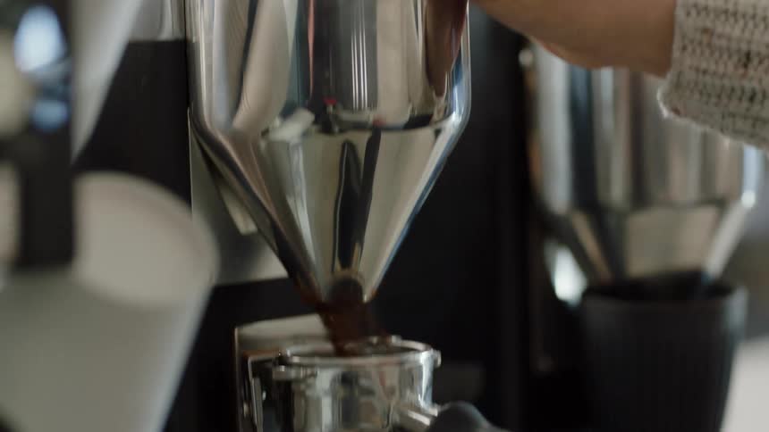 Woman presses a button on a coffee grinder causing the ground coffee to fill a portafilter