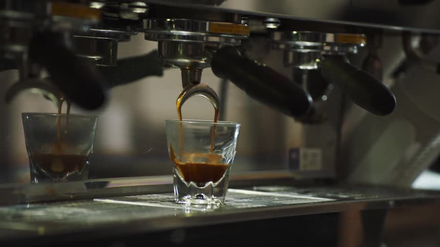 A cappuccino machine pouring cappuccino into a glass in a room with a person taking the glass