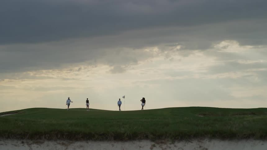 Four people stand on a golf course with dark skies overhead