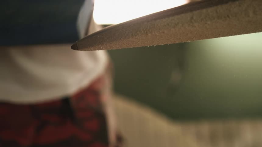 Man using sand paper over the surface of a surfboard inside a workshop