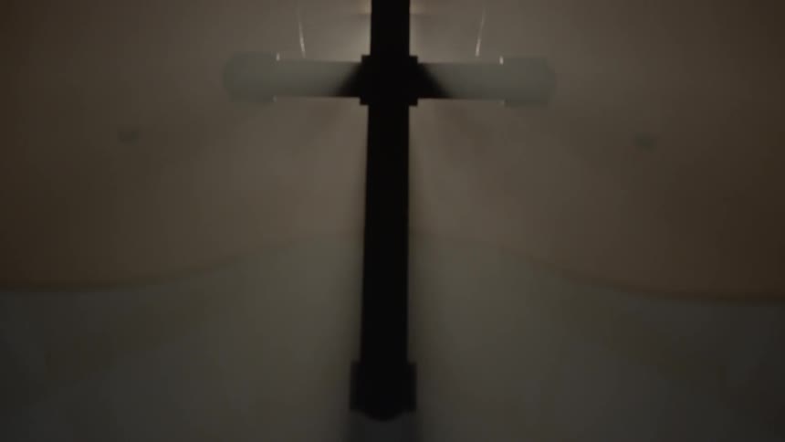 Lit candles in a church below a cross illuminated from behind