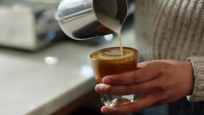 A person pouring cream into a cup of coffee