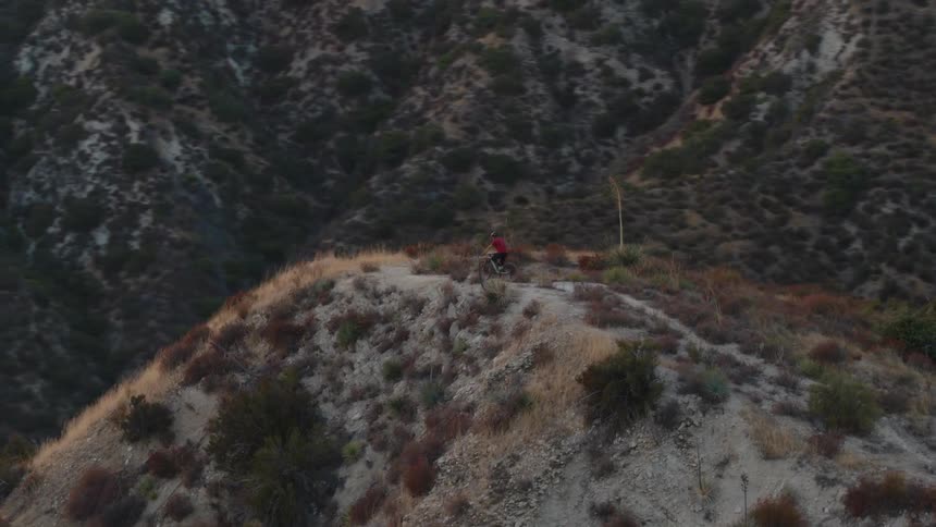 A mountain biker rides to the top of a brush covered mountain