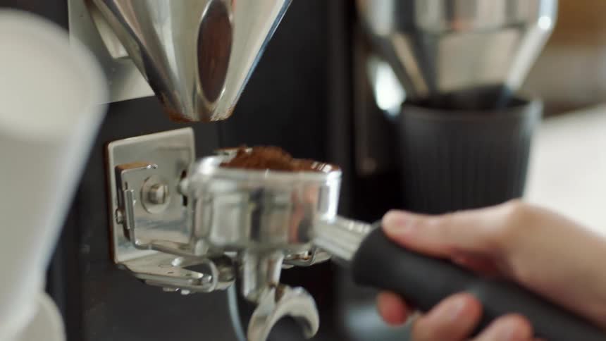 Person uses handle to move coffee grounds from under grinder in coffee shop