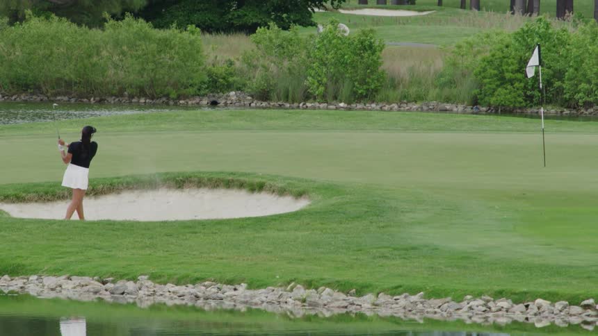 A female golfer hits a golf bowl out of a sand bunker