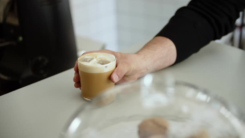 A person in a room taking a glass of iced coffee from a table