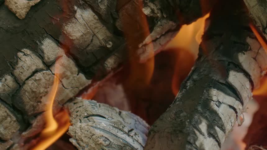 Flames are rising from the charred wood of a campfire