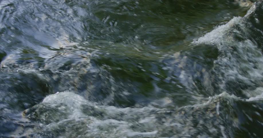 River water flows over rocks as sunlight shines and reflects on the surface