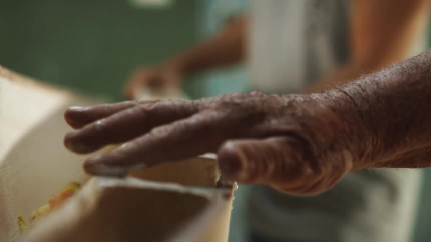 An elderly man applies wood glue to a crafting project while his hand is shaking
