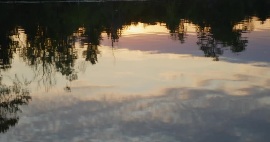 Water rippling with the reflection of trees the sky and clouds
