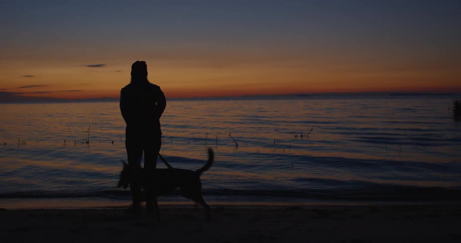A woman is trying to control her dog at the beach as the sun sets