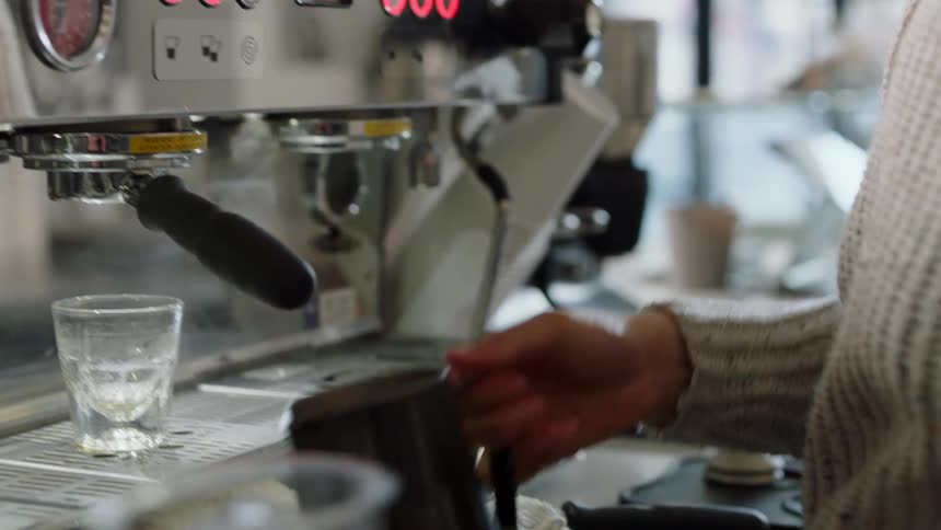 Woman with grey sweater uses coffee machine to make coffee in cafe