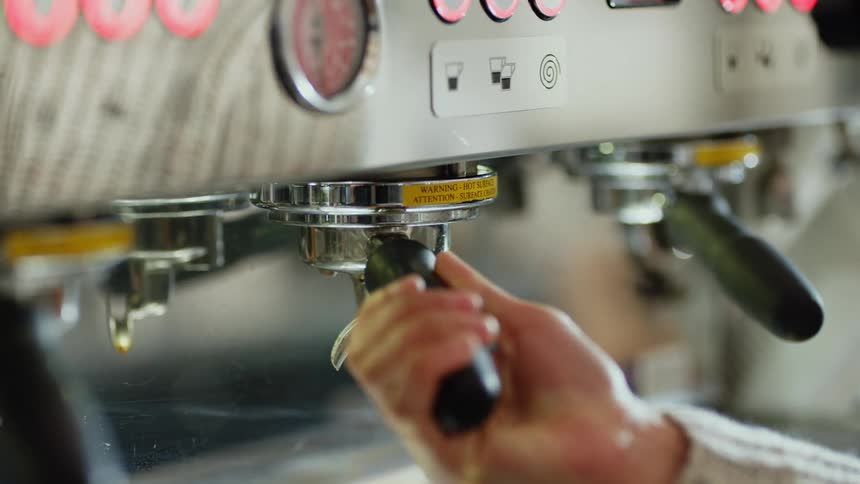 A hand attaches a handle to an espresso machine and turns it