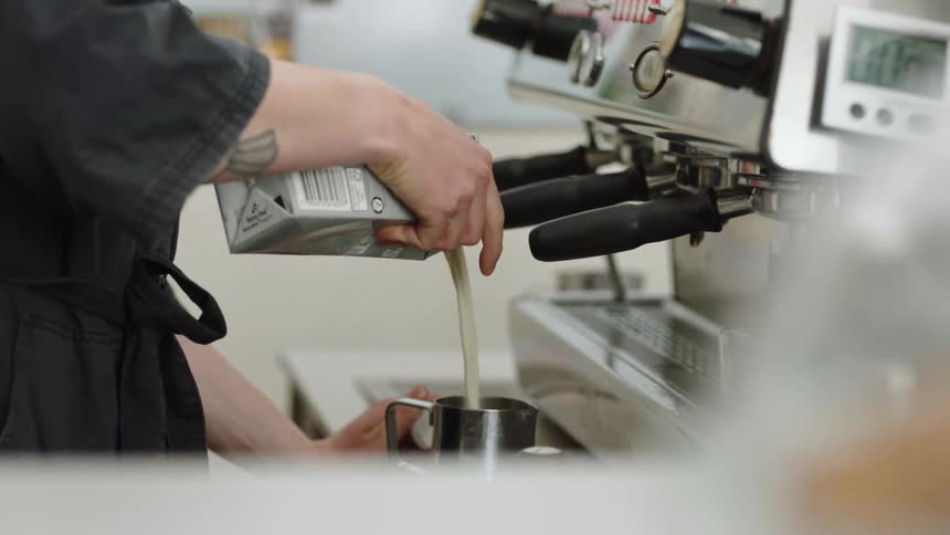 Barista pouring milk into a metal container in front of a espresso coffee machine