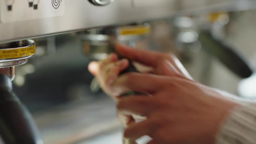 A person with a sweater in a room placing a handle on a cappuccino machine
