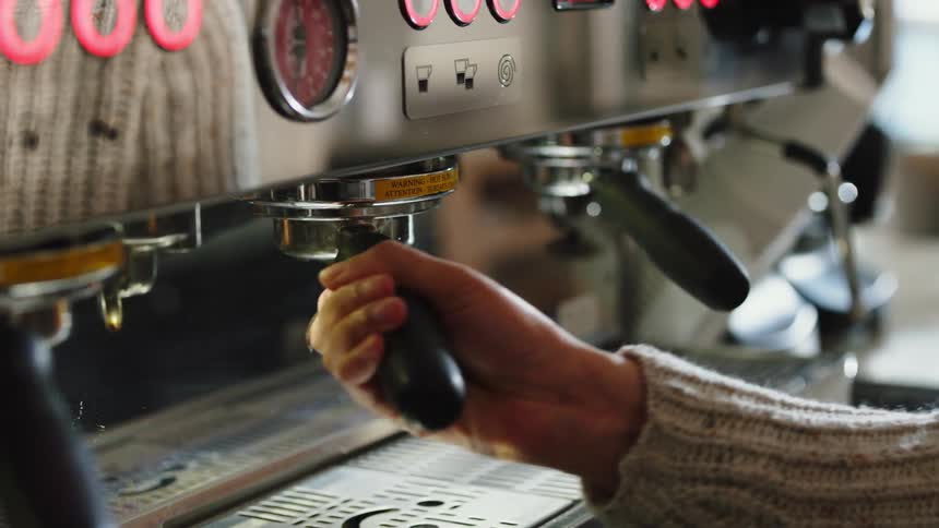 Barista wearing sweater attached handle to commercial coffee appliance