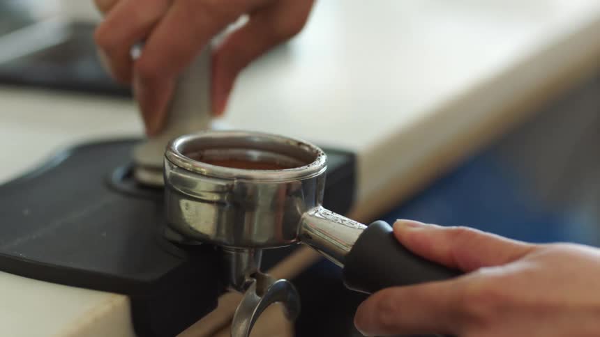 A barista brushes coffee grounds off the rim of an espresso machine coffee filter