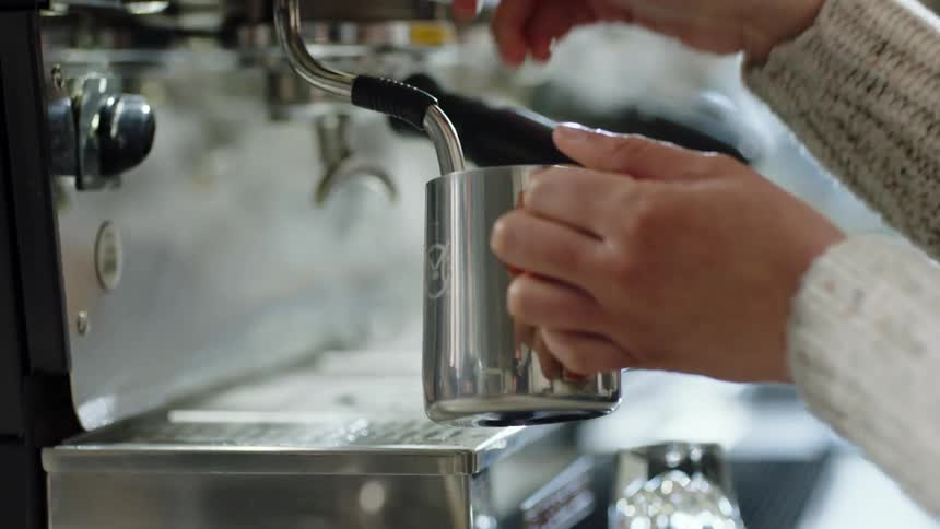 A person in a room with a sweater using a cappuccino machine and filling up a mug