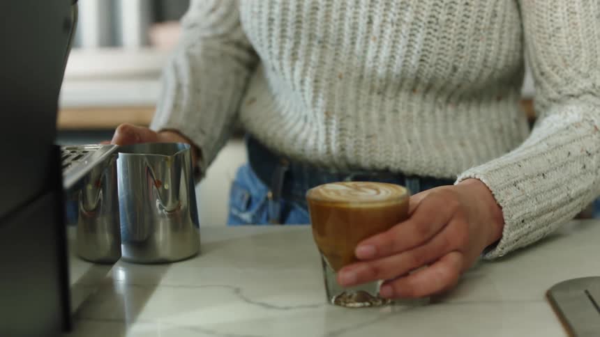 Barista serving a glass of espresso and milk with foam art atop