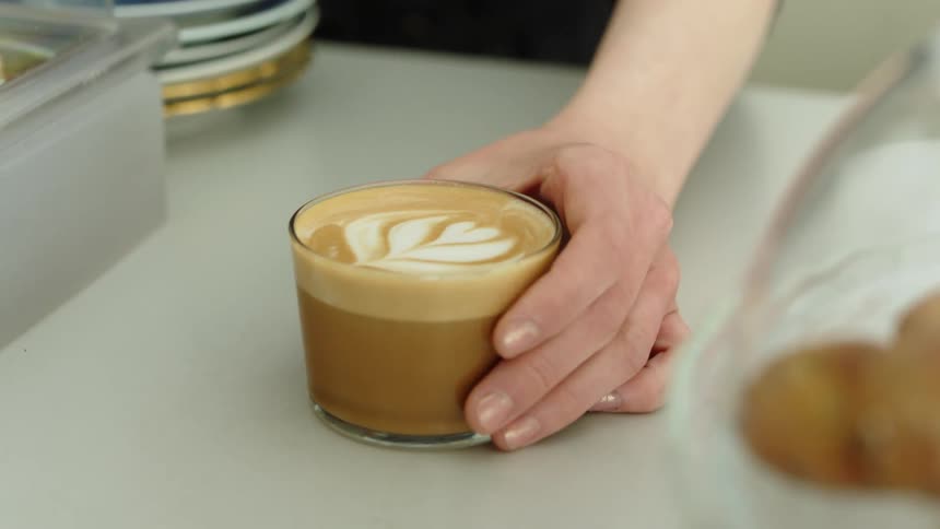 Womans hand puts latte with heart on counter in cafe