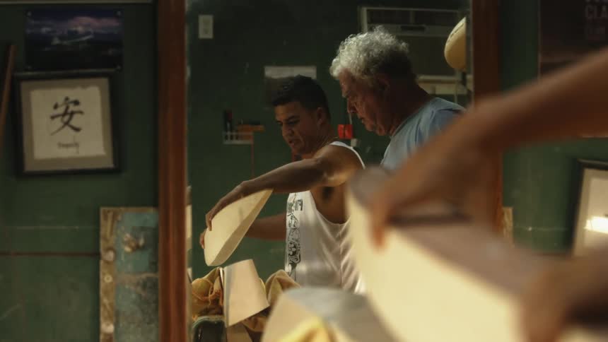 A father and son are looking over a surfboard design crafted in wood while indoors