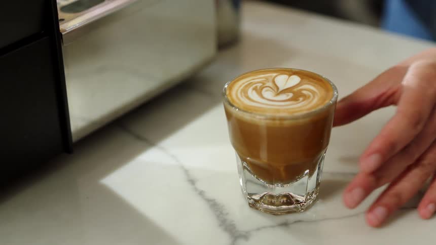 Mans hand puts a glass of latte with a heart