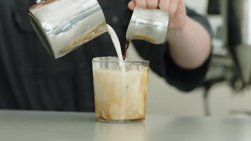 Barista pouring coffee and milk on a glass filled with ice cubes