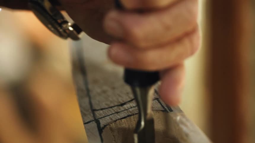 A person in a room with a wristwatch using a chisel on a piece of wood