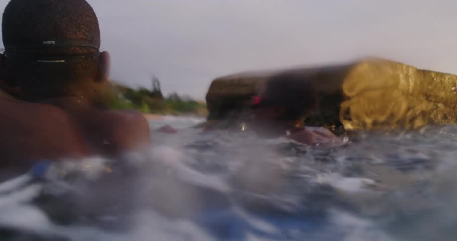 Two youths hang onto concrete slabs while bloating in water with shore in background