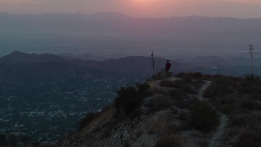 A person on a bicycle is on the top of a mountain watching the sun set over mountains in the distance