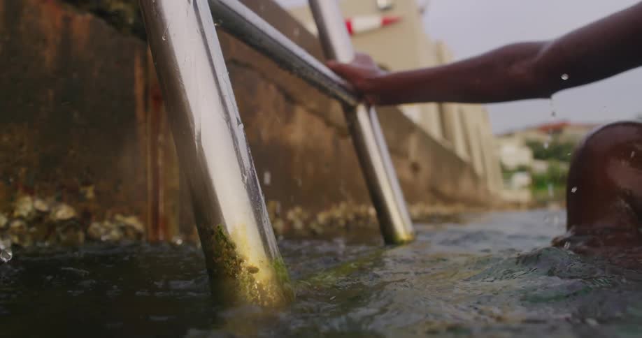 A man climbs out of the ocean using a ladder