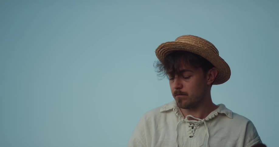 Young man wearing a straw hat painting with oil outdoors at evening