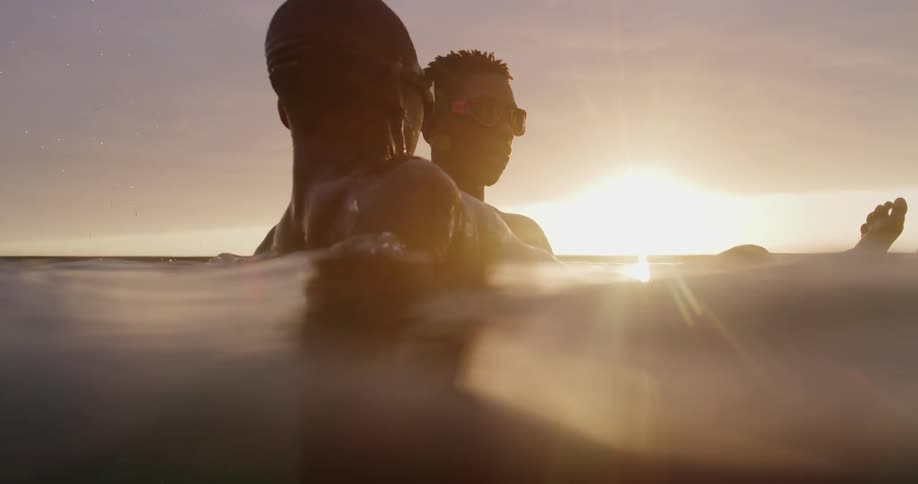 Young man teaching a woman how to float on the ocean waters at sunset