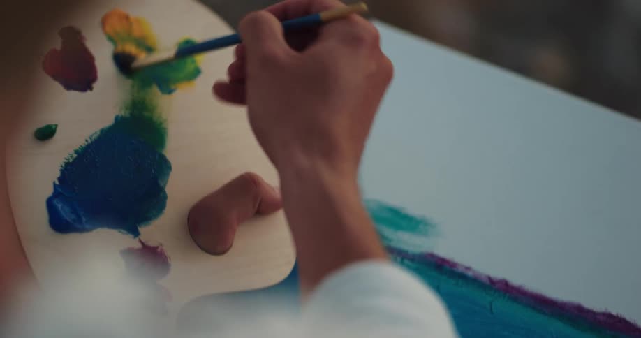 A woman mixes paint on a wooden palette with a paint brush