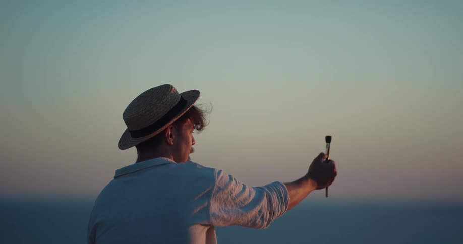A man raises a paint brush up at the sky