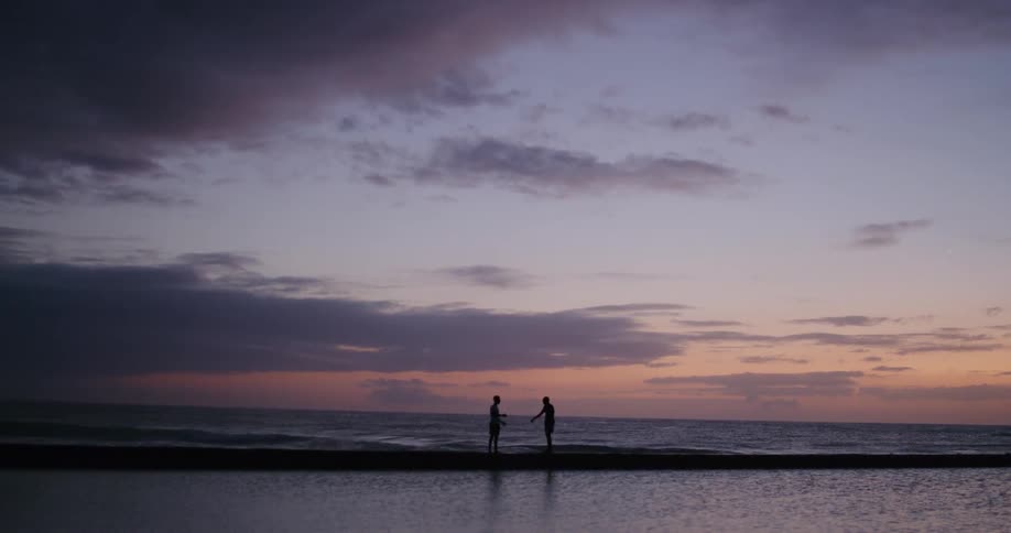 Two people are standing in the ocean water while the sun is setting