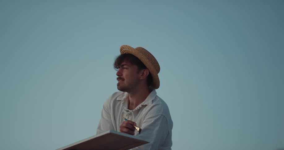 A man looks off in to the distance as he paints a picture outside