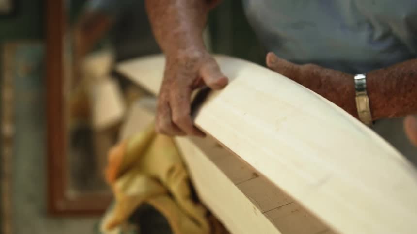 A man working on a surfboard of wood in a shop