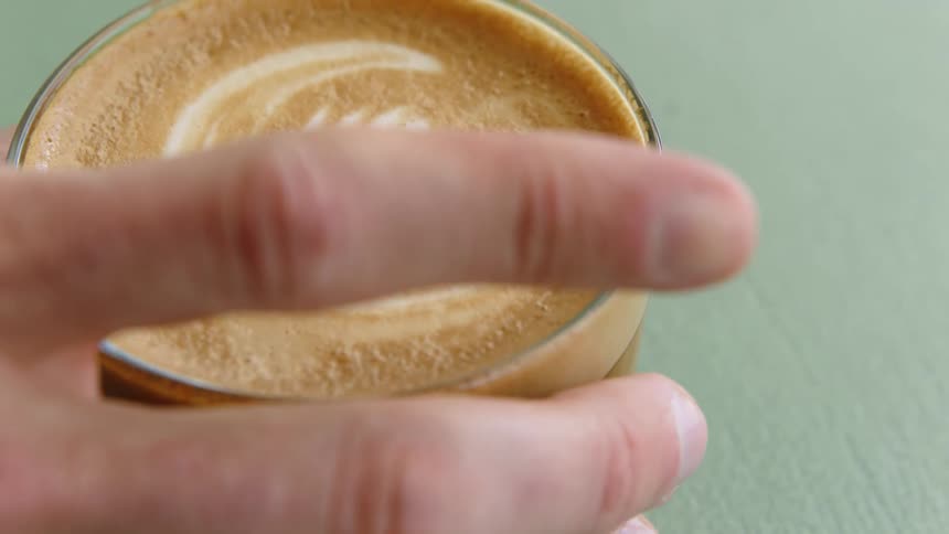 Person picks up glass of cappuccino with art in foam