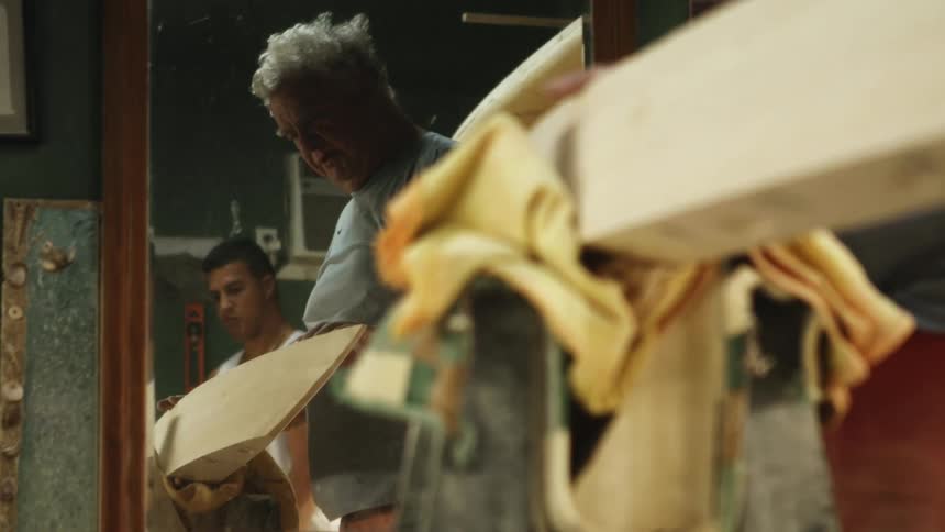 Two workers working on a handcrafted surfboard in a shop