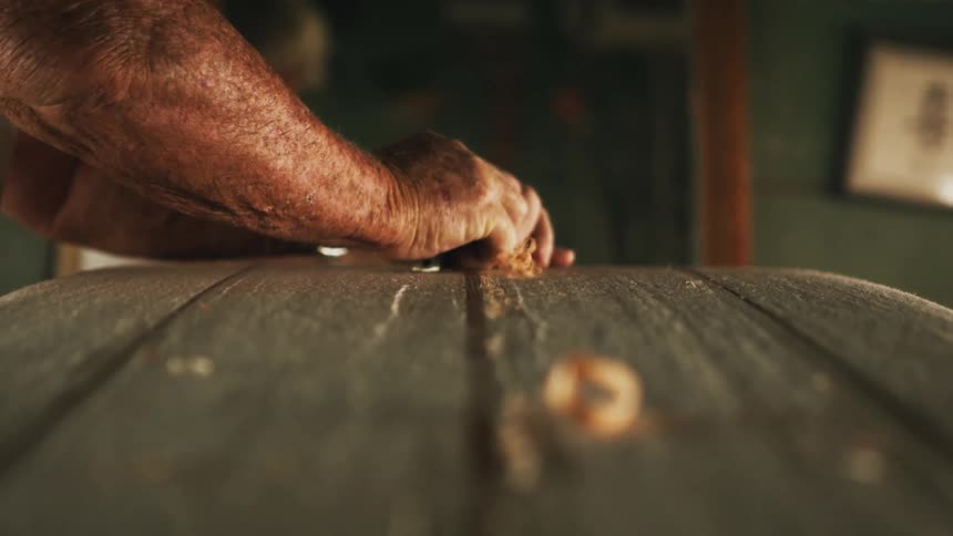 A man in a room using a tool on wood with a mirror and wall in the background