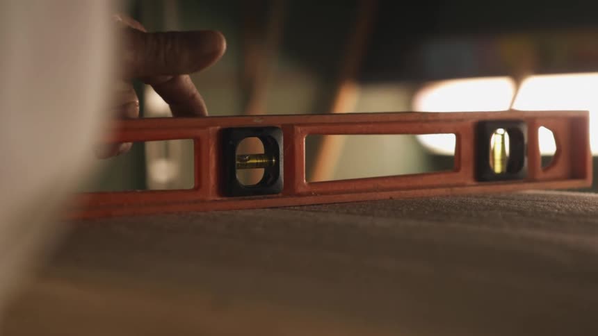 A man uses a spirit level to measure the levelness of a wooden surface indoors during the day