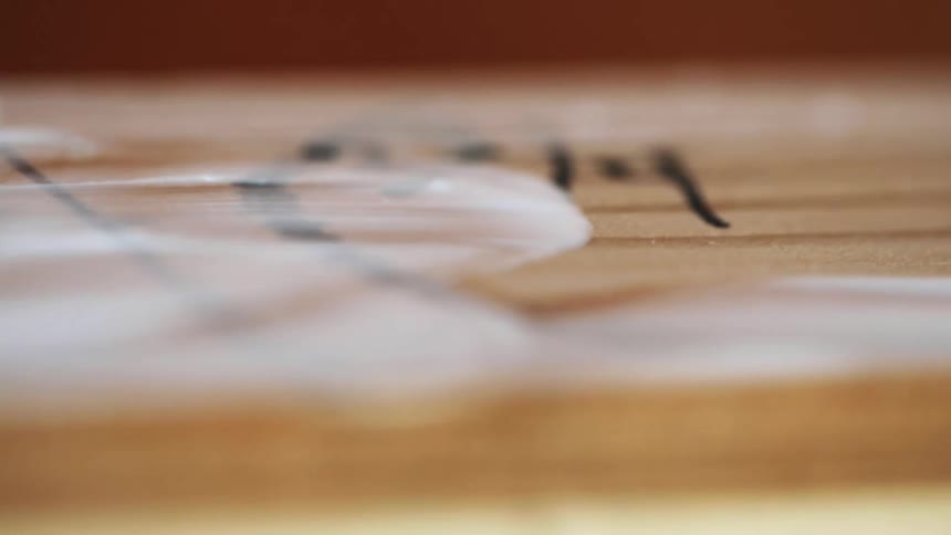 A person in a room using their finger to apply a white cream onto a piece of wood