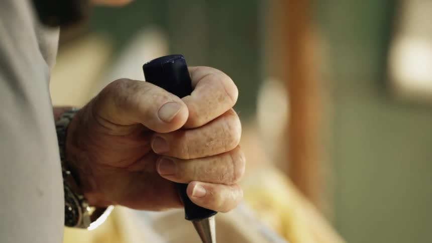 A mans hands holding a chisel and hitting it with a mallet