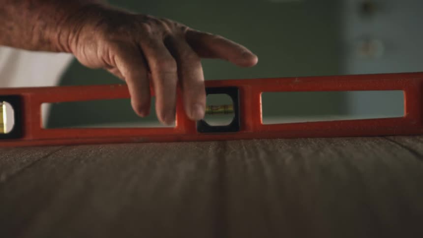 A person in a room using a leveler tool with a wall in the background