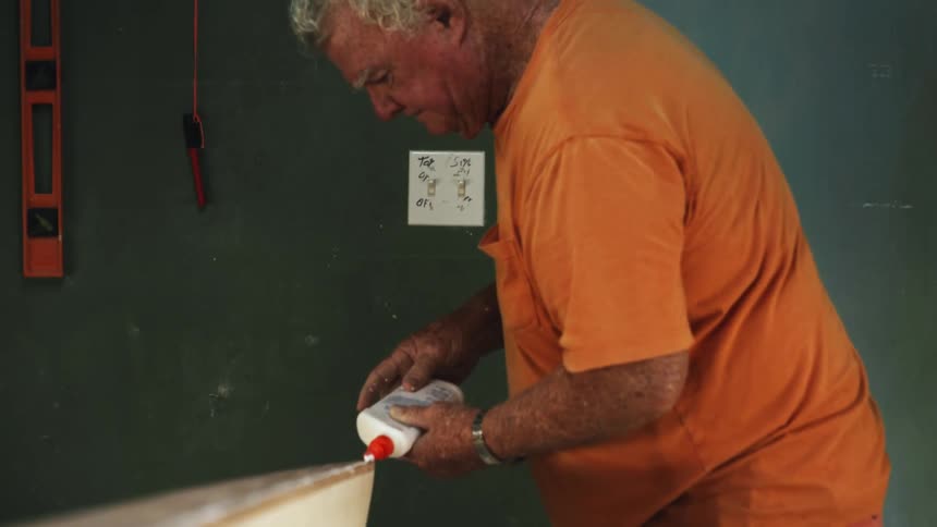 Man wearing orange glues wooden pieces together standing in workshop