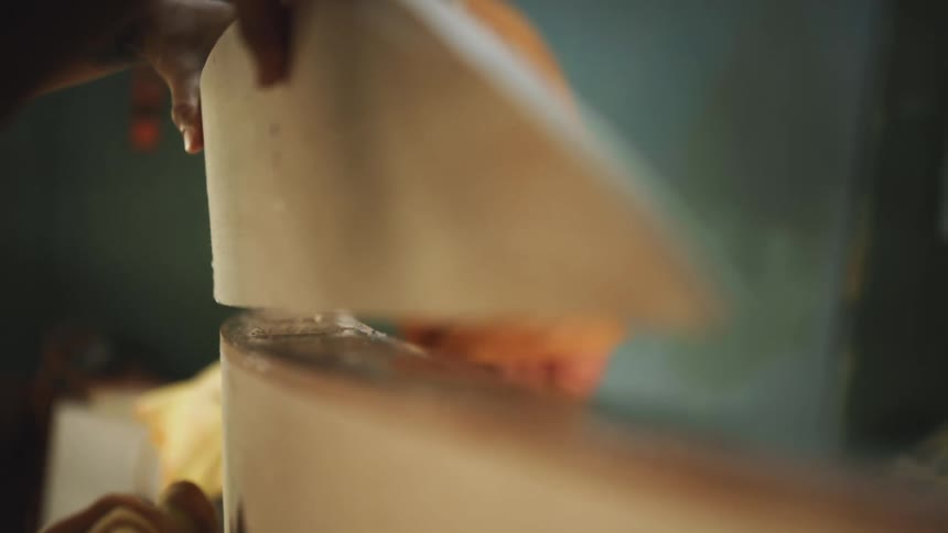 Man gluing together two halves of a surfboard inside a workshop