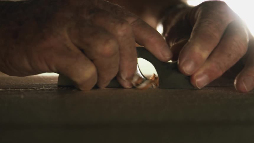 A man uses a hand planer causing curls of wood
